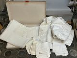 une valise remplie de serviettes et de serviettes de table blanches posée par terre