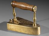 an antique brass iron with a wooden handle on a gray surface