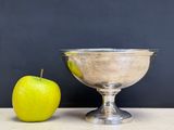 a green apple next to a silver bowl on a table