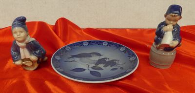 two figurines sitting next to a plate on a red cloth