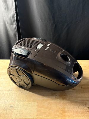 une photo d'un aspirateur noir posé sur une table en bois