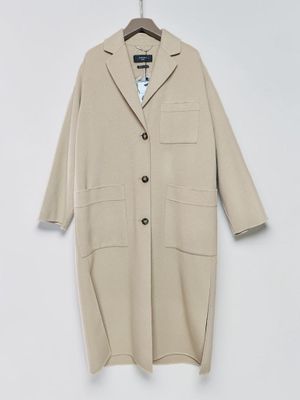 a beige coat hangs on a hanger against a white wall
