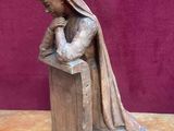 statue en bois représentant une femme assise sur un banc, les mains jointes au-dessus de la tête