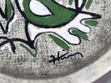a green bird painted on a plate on a table