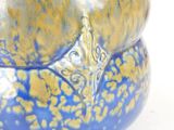 a close up of a blue and gold vase on a white surface