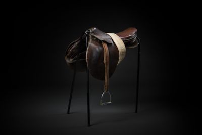 the saddle of a horse on a stand against a black background