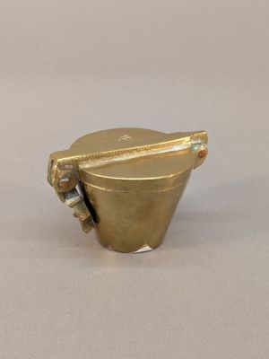 une image représentant une tasse en laiton avec une anse, posée sur une surface blanche