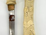 two pieces of carved ivory and a knife on a white surface