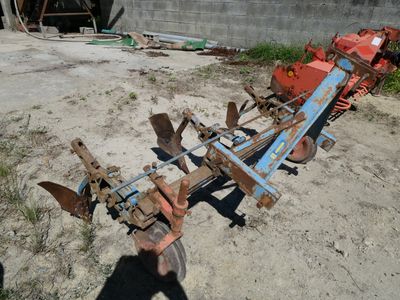 a tractor plow sitting in the dirt in front of a building