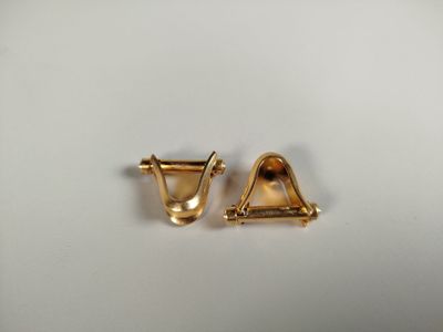 une paire de boucles d'oreilles en or sur une surface blanche