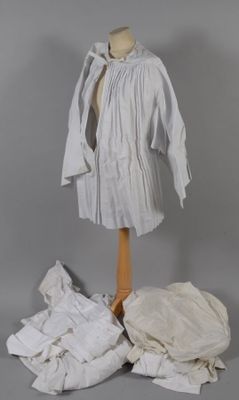 un mannequin vêtu d'une chemise blanche et entouré d'une pile de vêtements