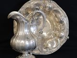 an antique silver plate with a silver pitcher on a black background