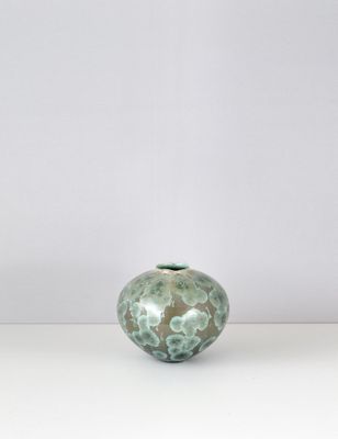 un vase vert et blanc posé sur une table blanche, sur fond blanc