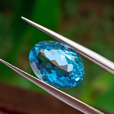 a close up of a blue topaz gemstone being held by a pair of tweets