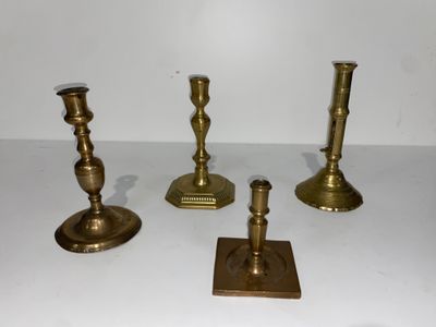 quatre bougeoirs en laiton posés sur une table blanche, sur fond blanc
