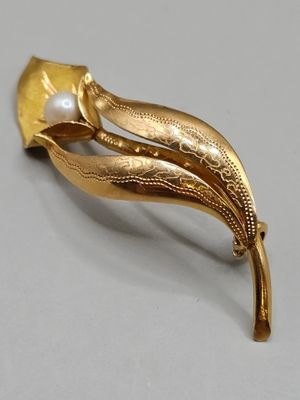 an image of a gold brooch with a pearl in the center