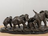 statue of a herd of elephants walking across a wooden surface