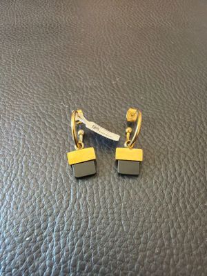 une paire de boucles d'oreilles noires et dorées posées sur une surface en cuir noir