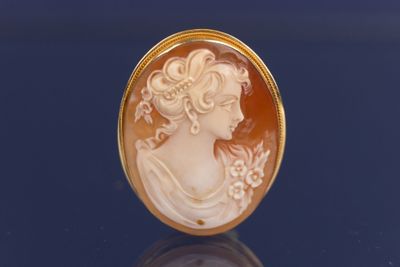 Une broche plaquée or représente le profil d'une femme.