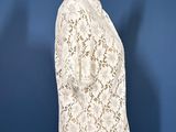 a white lace jacket on a mannequin stand against a blue background