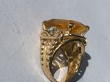 a gold ring with a yellow stone on a white surface