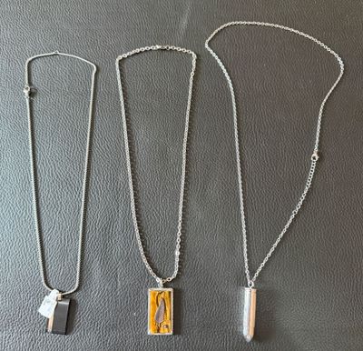 three silver and gold necklaces sitting on top of a black surface