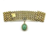 a close up of a gold bracelet with a green stone