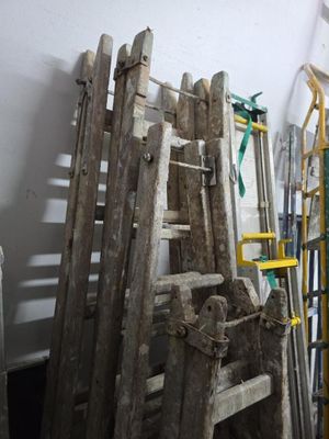 un tas de vieilles échelles en bois près d'un mur blanc