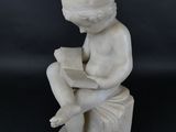 statue en marbre représentant un garçon en train de lire un livre, assis sur un tabouret