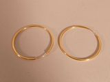 two pairs of gold hoop earrings sitting on top of a white surface