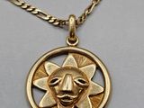 a close up of a gold necklace with a sun in the middle