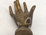 brass statue of a hand holding a coin on a white surface
