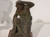statue of a woman sitting on a stone block with a shadow of a man in the background