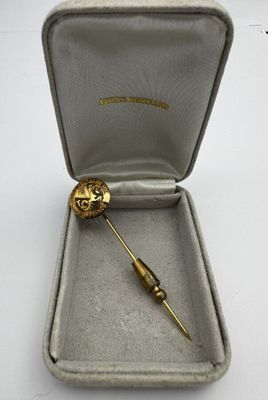 a small gold brooch in a box on a white surface