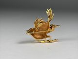 an image of a gold bird broochle on a white surface