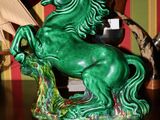 une statue de cheval verte posée sur une table, avec un bateau en arrière-plan