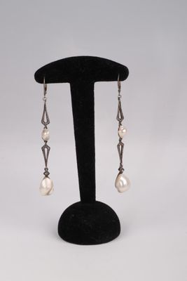 a pair of pearl and silver earrings on a black stand