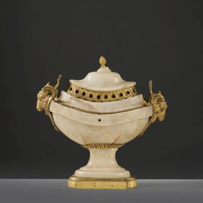 a white and gold vase with a lid on a table