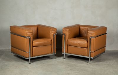 two brown leather chairs sitting next to each other on a cement floor