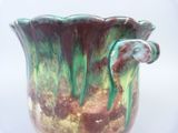 a green and brown vase sitting on a white surface