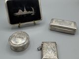 trois objets en argent, dont un briquet, une boîte et une image représentant un bateau