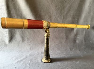 un télescope ancien en laiton muni d'une poignée en bois, sur fond gris