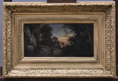 une peinture à l'huile représentant un paysage, dans un cadre doré, posée sur une table en bois
