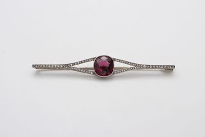 un gros plan d'une bague en pierre rouge et diamants posée sur une surface blanche