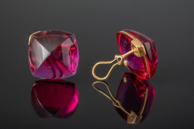 une paire de boucles d'oreilles en verre rouge et violet posées sur une surface noire