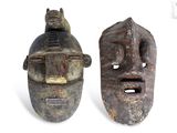 pair of wooden masks with faces and a cat sitting on top of them