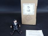 une petite figurine représentant un homme en costume assis à côté d'une boîte
