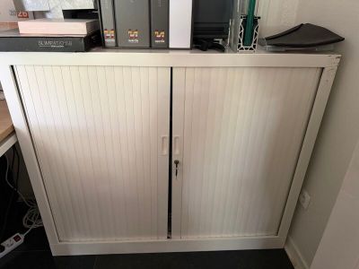 une armoire blanche à deux portes, sur laquelle est posé un micro-ondes