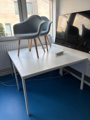 une table blanche avec deux chaises, placée devant une fenêtre
