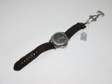 une image représentant une montre posée sur une surface blanche, à laquelle est attachée une étiquette